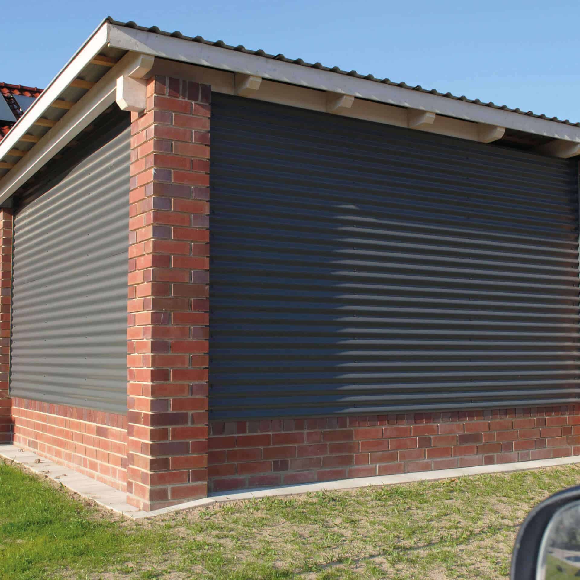 Een moderne garage met metalen golfplaten en stevige bakstenen pilaren. De donkere metalen golfpanelen zorgen voor een robuuste en stijlvolle look.