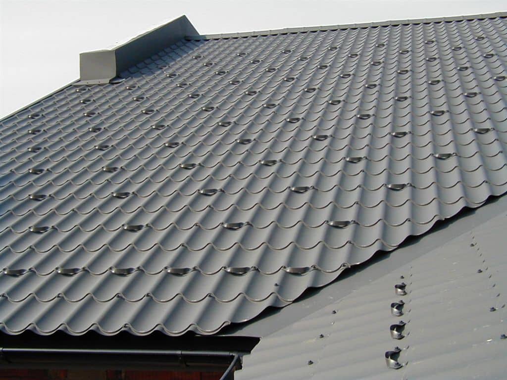 Dak met donkergrijze metalen dakpanplaten, netjes gemonteerd met zichtbare bevestigingsschroeven.