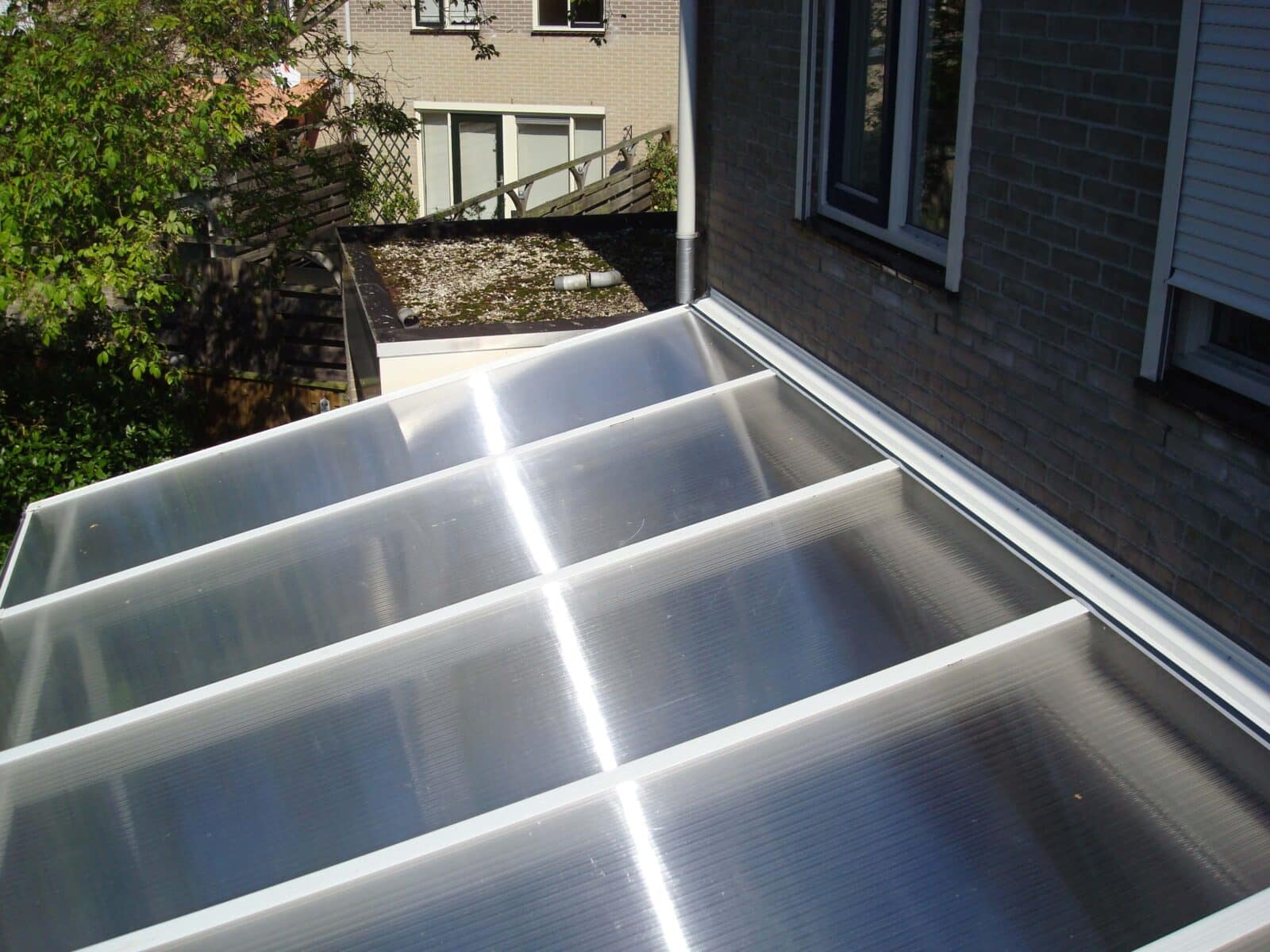 Bovenaanzicht van een overkapping van heldere kanaalplaten met witte montage profielen, zichtbare reflectiestrepen door de zon.