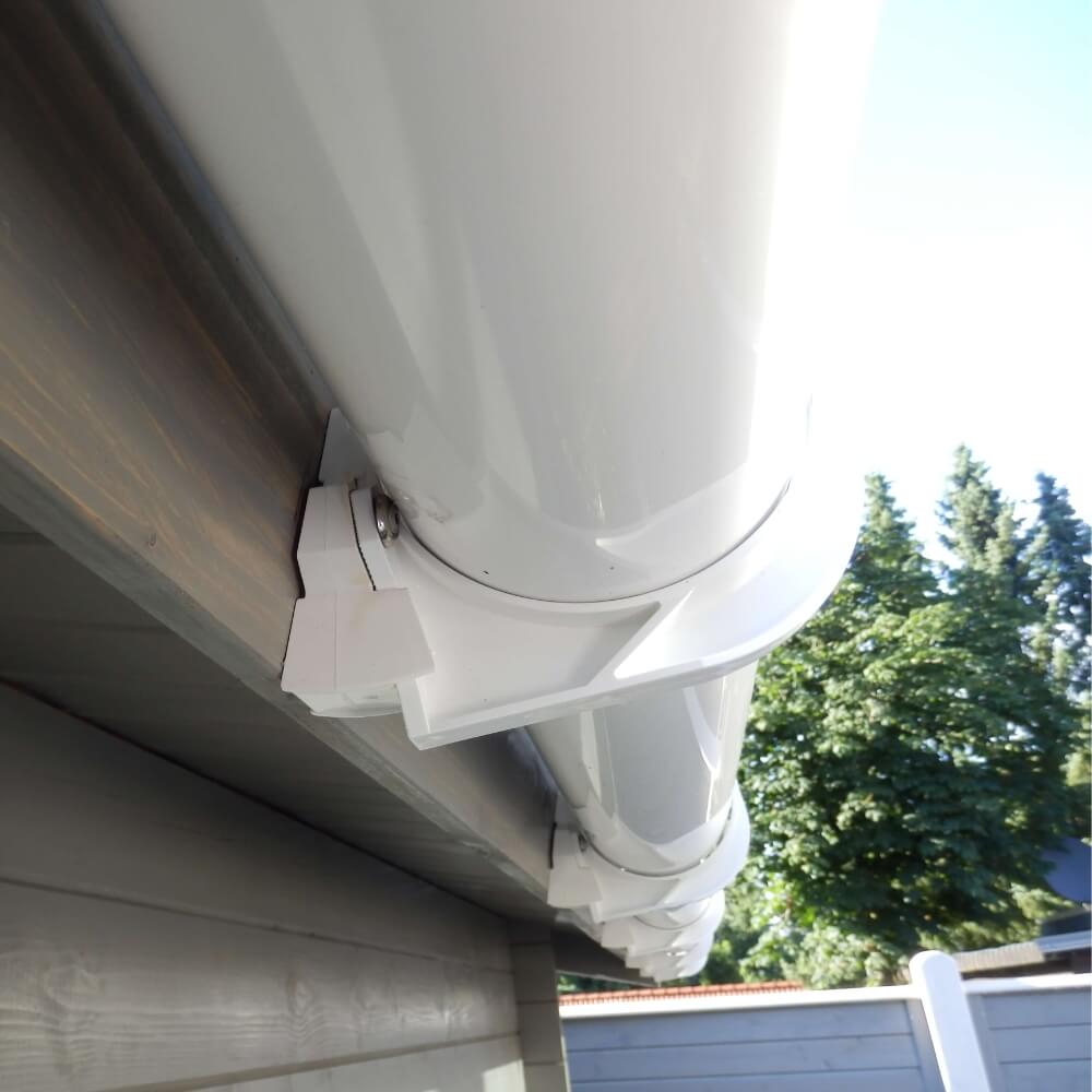 Installatiedetail van een witte regengoot op het huis, met het verbindingsstuk en de beugel