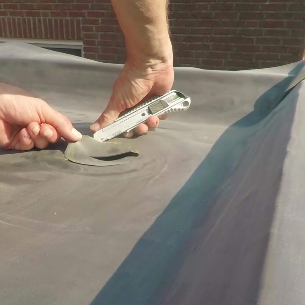 Een persoon voert een reparatie uit aan een EPDM dakbedekking door een stuk beschadigd membraan uit te snijden met een cutter
